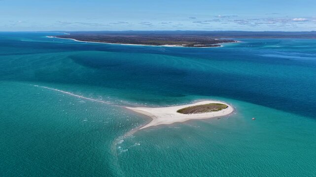 Aerial view of Pelican Bank with sparse vegetation surrounded by turquoise and deep blue bay waters near K'gari Fraser Island, Hervey Bay, Queensland, Australia.