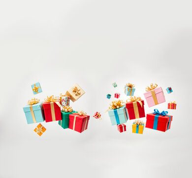 large group of colorful presents with ribbons flying and floating in the air against a plain wall in a studio.