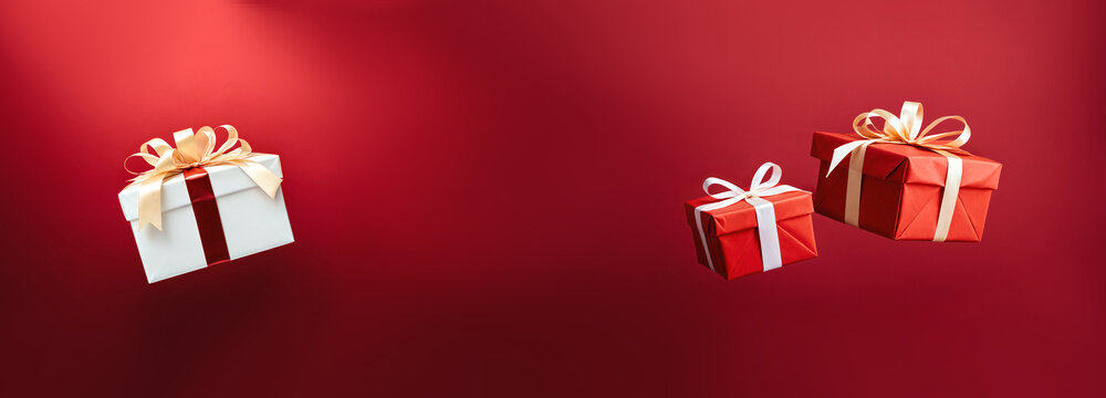 white box with ribbon and two red presents flying floating and falling in the air against a dark wall in a studio.