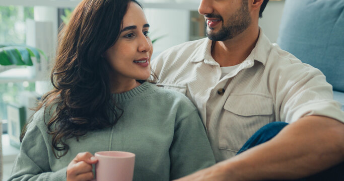 Happy young adult Hispanic couple drinking coffee and relaxing sit on floor in living room at home. Domestic lifestyle, positive weekend leisure, cheerful relationship bonding, family love concept.