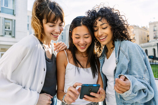Young multiracial women friends checking their phones together outdoors in the city. Friendship and technology concept.