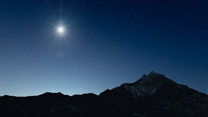 Fototapeta premium Glowing Christmas star above a peaceful mountain landscape