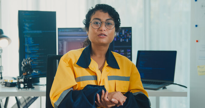 Young African American female robotics engineer discussing mechanical part on video call and looking at camera in laboratory. Remote work, virtual training, online meeting, future technology concept.