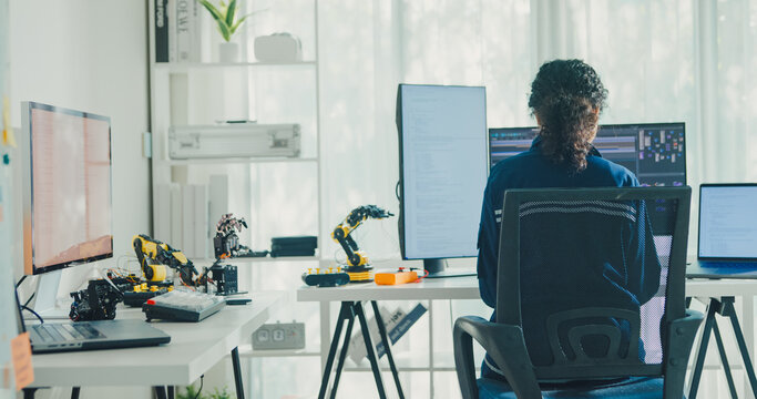 Young African American female robotics engineer coding AI software for robotic arm in laboratory. Embedded system, firmware testing, machine learning, industrial automation, future technology concept.