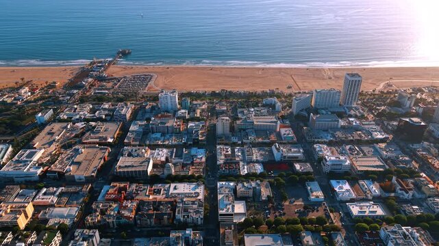 Santa Monica waterfront blocks and pier from above. An elevated view looks across rooftops toward the sandy shore and sunlit ocean.