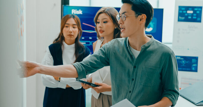 Group of Asian businesspeople work together collaborating and sharing ideas use colorful note on wall in business meeting in office. Financial generation z team brainstorm on e-Commerce project.