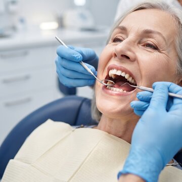 A senior woman opens her mouth wide while a dentist examines her teeth with a mirror and probe during a routine checkup at a dental clinic.