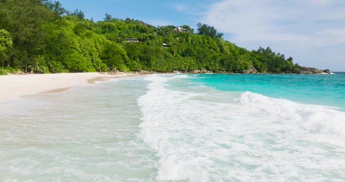 Clear turquoise waters wash up on a pristine white sandy beach, bordered by lush greenery. Seychelles, Mahe. Anse Intendance.