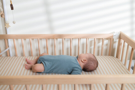 Baby lying flat on back inside a wooden nursery crib