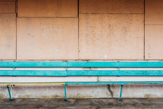 Un long banc bleu devant un mur rose orang&eacute;. Un vieux banc en bois de gare devant un mu d&eacute;cr&eacute;pi.