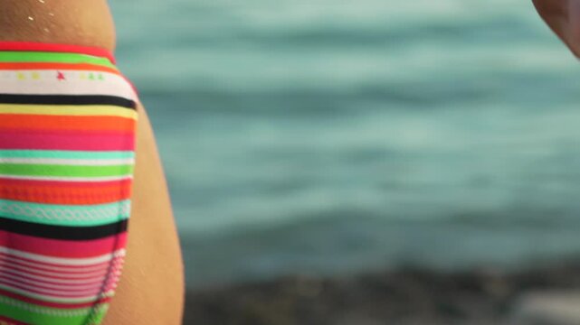 Colorful bikini bottom detail of woman walking into sea water during summer vacation. Medium panning shot.