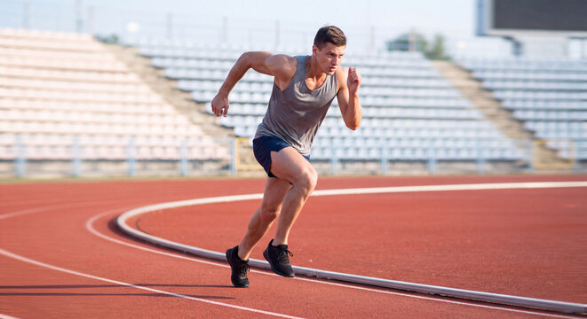 Energetic male sprinter in sports clothes running along an athletic track outdoors on a sunny day during rigorous stamina and cardio training