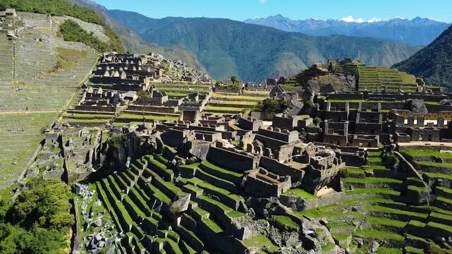 Aerial view of Historic Sanctuary of Machu Picchu featuring ancient stone ruins and agricultural terraces set against lush green mountains in Urubamba Province, Cusco, Peru.