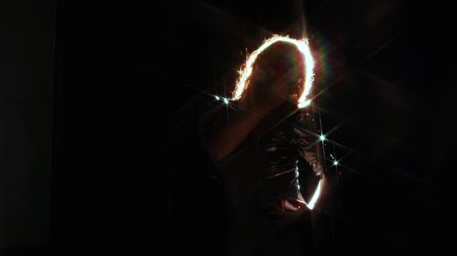 Bright light beam covering the face of a woman in a shiny dress. Anonymous figure, star flare and dark space for themes of energy, insight and change.