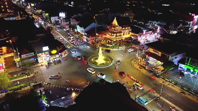Aerial view of Tugu Yogyakarta Monument illuminated at night with busy traffic and city lights surrounding the historic landmark in Yogyakarta, Special Region of Yog, Indonesia.