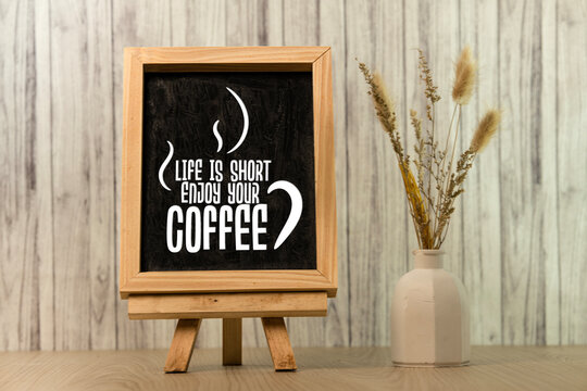 Chalkboard sign with Life is Short Enjoy Your Coffee quote on a wooden easel with dried flowers