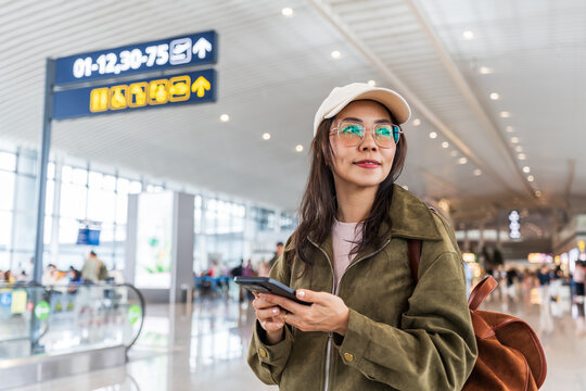 Female tourist passenger is checking messages on her phone and looking for her gate at the airport