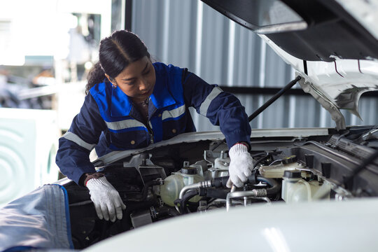 Female automotive technician inspecting vehicle under the open hood in professional workshop, car maintenance, mechanical service, skilled labor and automotive repair technology.