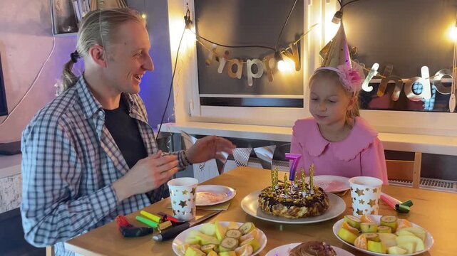 Father and daughter home celebrating birthday together with cake and fairy lights