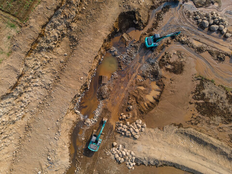 Mining Work of Excavators Operating on Muddy Terrain in a Large-Scale Rock and Sand Quarry in Dawuhan Kulon, Central Java, Indonesia. Heavy Machinery Works Across Wet Ground Viewed from Above.