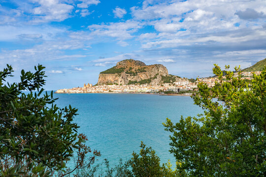 scenic view coastal town of Cefalu Italy Sicily framed by lush green foliage under a summer sky picturesque landscape