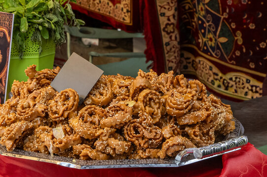 Sweet chebakia pastries, a traditional moroccan dessert made with honey and sesame, are displayed on a silver tray at a vibrant street market, reflecting rich gastronomy and local culture