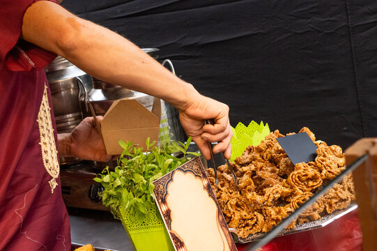 Vendor's hand serving traditional moroccan chebakia pastry, also known as m'kharqa, from a food stall, highlighting local gastronomy and cultural market experience