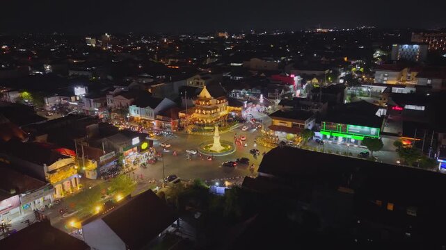 Aerial view of the illuminated Tugu Yogyakarta Monument surrounded by city streets and night traffic in Yogyakarta, Special Region of Yog, Indonesia.
