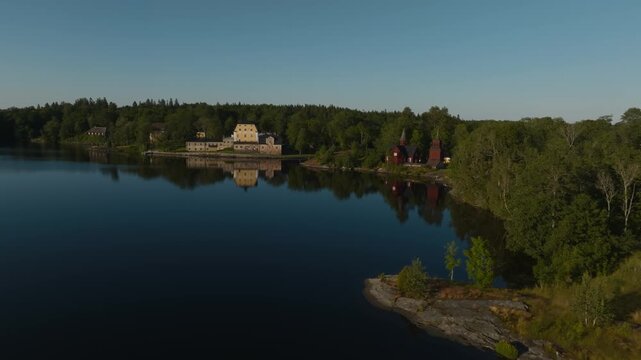Panoramic drone shot of Fagervik manor house and wooden church by lake, Finland