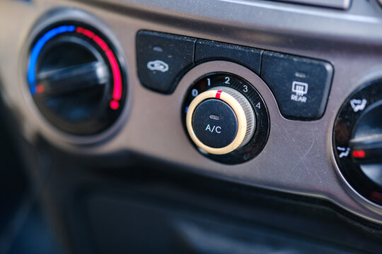 Close-up of manual climate control knobs and air conditioning button on a car dashboard panel inside a modern passenger vehicle