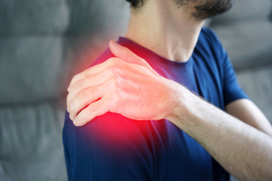 Shoulder tendinitis concept. Unidentified man touching sore shoulder with hand in tendinitis pain with red highlight