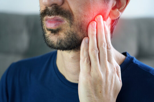 Young man touching jaw and grinding teeth in severe wisdom tooth pain