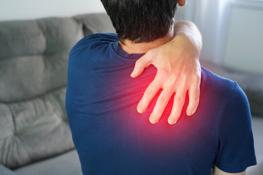 Man squeezing muscle with hand suffering from trapezius pain. Red highlight pain area.