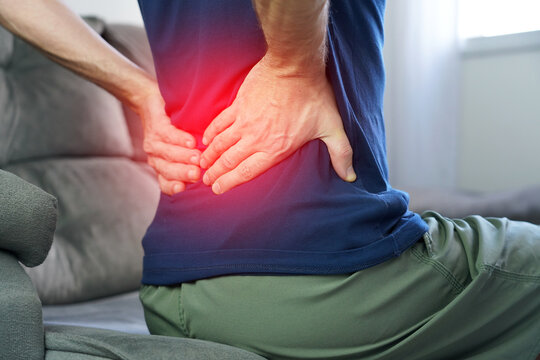 Lumbalgia or lower back pain concept. Unrecognizable man pressing hands against lower back in severe lumbalgia pain with red highlight.
