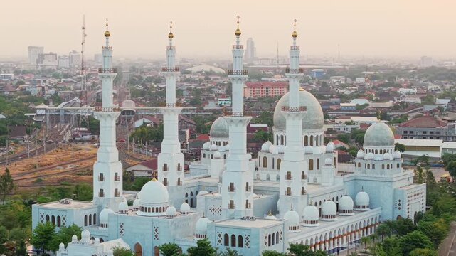 Aerial view of the Sheikh Zayed Grand Mosque featuring white domes and minarets surrounded by the urban landscape of Surakarta, Central Java, Indonesia.