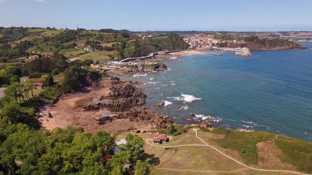 Drone view of Asturian shoreline in Spain. Atlantic ocean, rocky coastline, green hills and Candas town skyline 