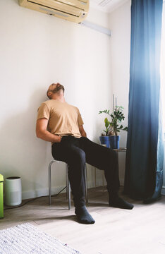 Exhausted Man Sitting on a Stool Leaning Against the Wall at Home