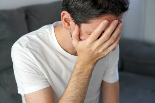 Unrecognizable man covering face and pressing eye suffering from severe chronic migraine