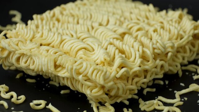 Uncooked instant ramen noodle block with crumbs on black background