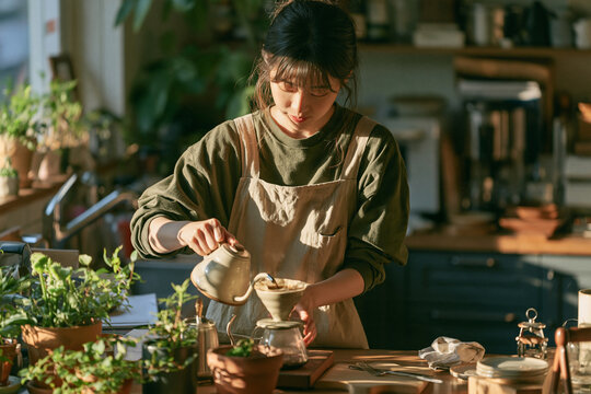 Korean woman making pour over coffee at a sunlit home kitchen counter