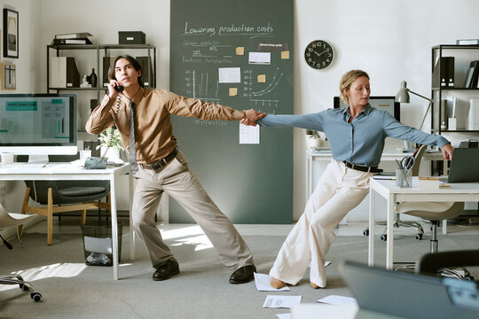 Young adult Caucasian businessman and businesswoman dancing while holding hands in office. Image suitable for workplace fun, corporate culture and teamwork concepts