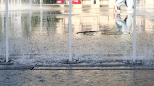 Low angle close up of ground fountain with water jets and people walking in background in sunny urban public space