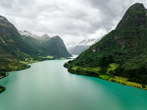 Aerial view of Oldevatnet lake with its turquoise glacial water surrounded by steep green mountains and lush forests under a cloudy sky Stryn Municipality, Vestland, Norway.