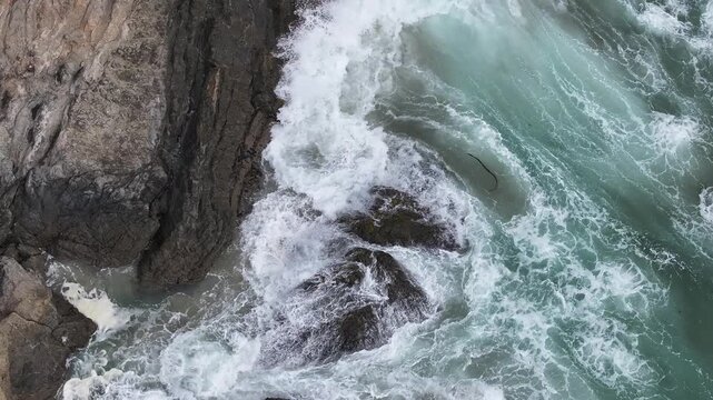 Aerial view of crashing waves against dark rocks along the rugged coastline in Fort Bragg, California, United States.