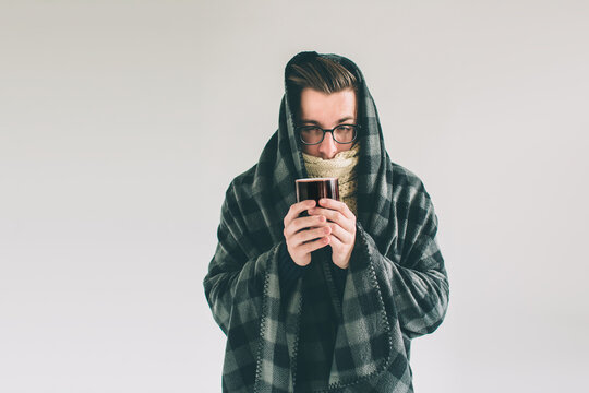 wrapped in the warm blanket or plaid, sick, young snotty man in glasses drinking warm healing tea.