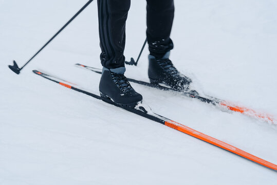 unrecognizable skier does skiing in snowy field, black clothes, orange skis and ski poles in hands, cloudy winter day, healthy lifestyle