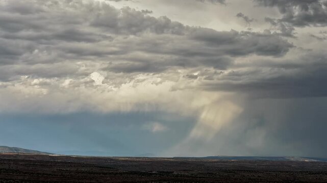 Aerial view of a single rain shower dancing over a mesa landscape as the sun illuminates the terrain in White Rock, NM, United States.