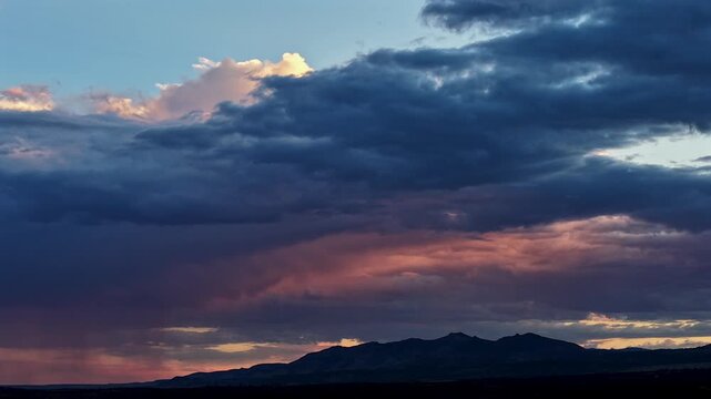 Aerial view of sunset light hitting a moving multi layered rain cloud with a white crest over the mountains in Los Alamos, New Mexico, United States.