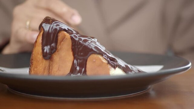 Close-up of a person taking a spoonful of delicious cheesecake topped with rich chocolate syrup, cinematic footage.