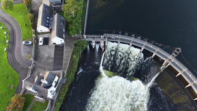 Aerial view of Salmon Weir releasing turbulent water into the River Corrib beside historic buildings and green parkland in Galway City Ireland.